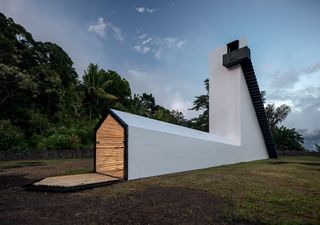 An abstractly designed white residential house with a bkack door opened using a drawbridge-style mechanism showcasing interior straw wall linings