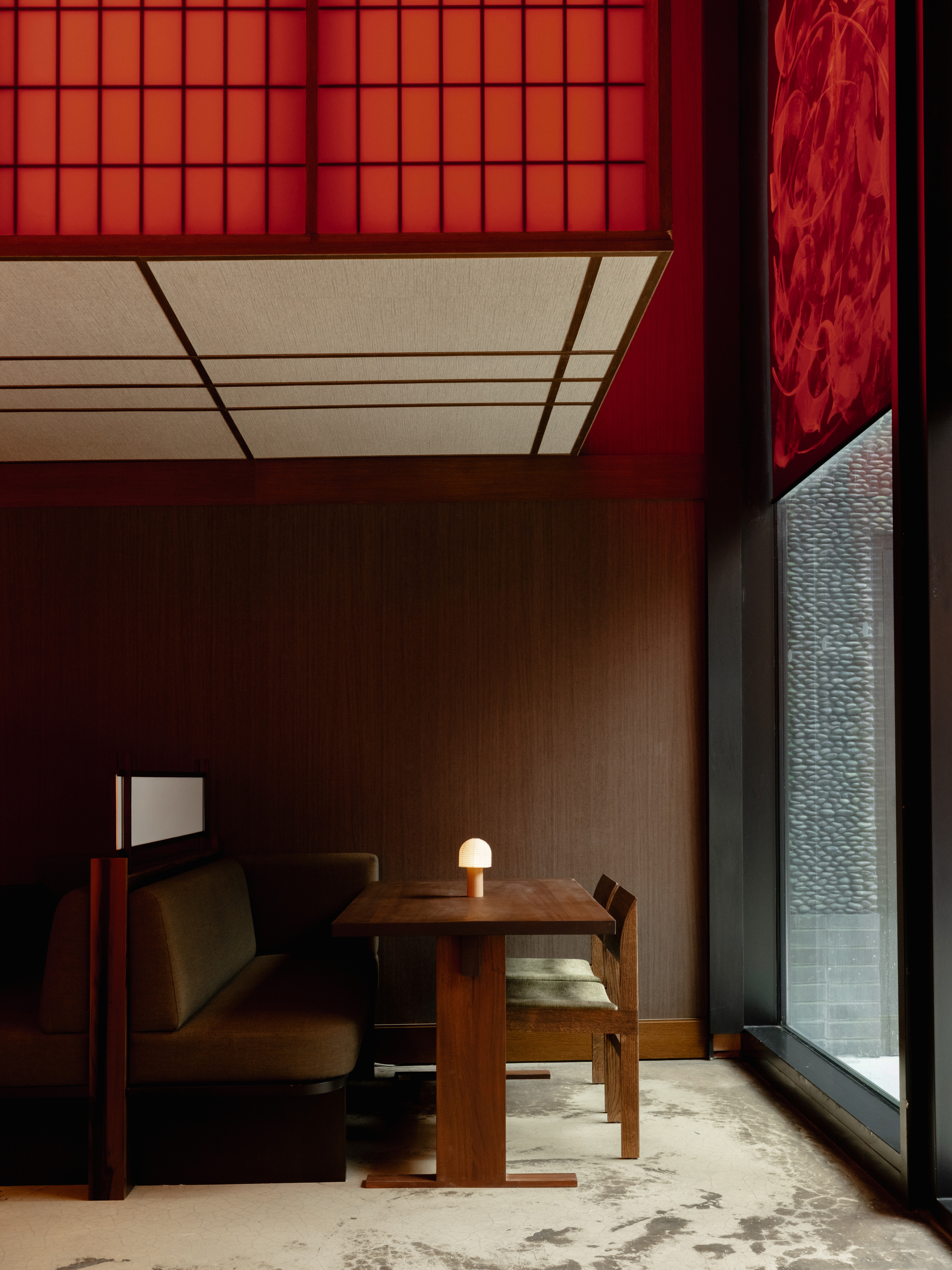 An asian-inspired restaurant dining room with sage green velvet seating booths, wooden furniture, and a paper panel ceiling with red and wood detailing.