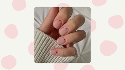 Curled hand with neutral nail polish base and a red dot towards the cuticle, on a neutral background with big pink polka dots