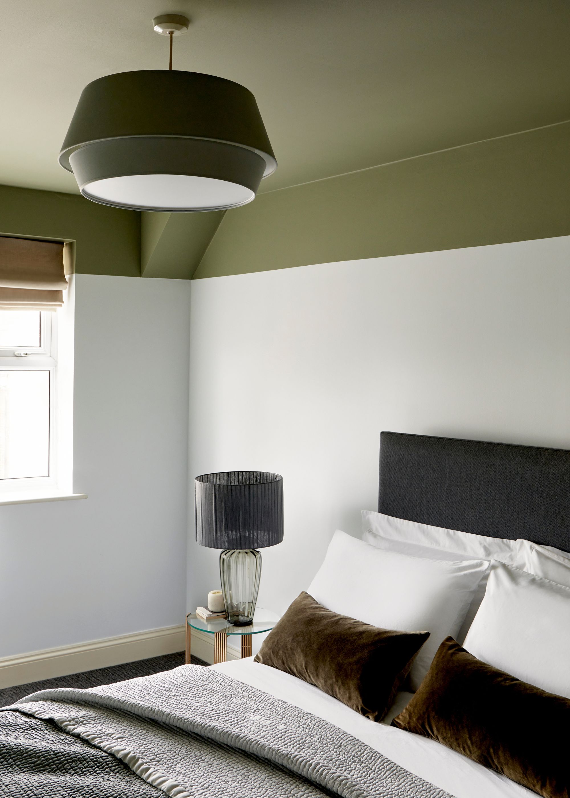 A modern bedroom with an olive green ceiling and upper portion of the wall, white paint on the rest of the walls, a black headboard, and neutral bedding.