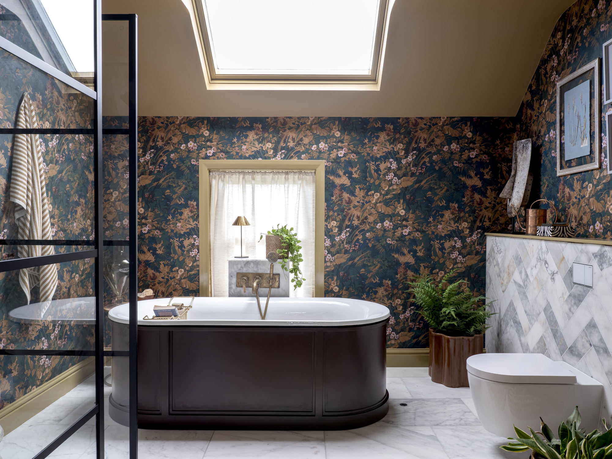 a bathroom with a traditional freestanding bath and floral wallpapered walls with a skylight