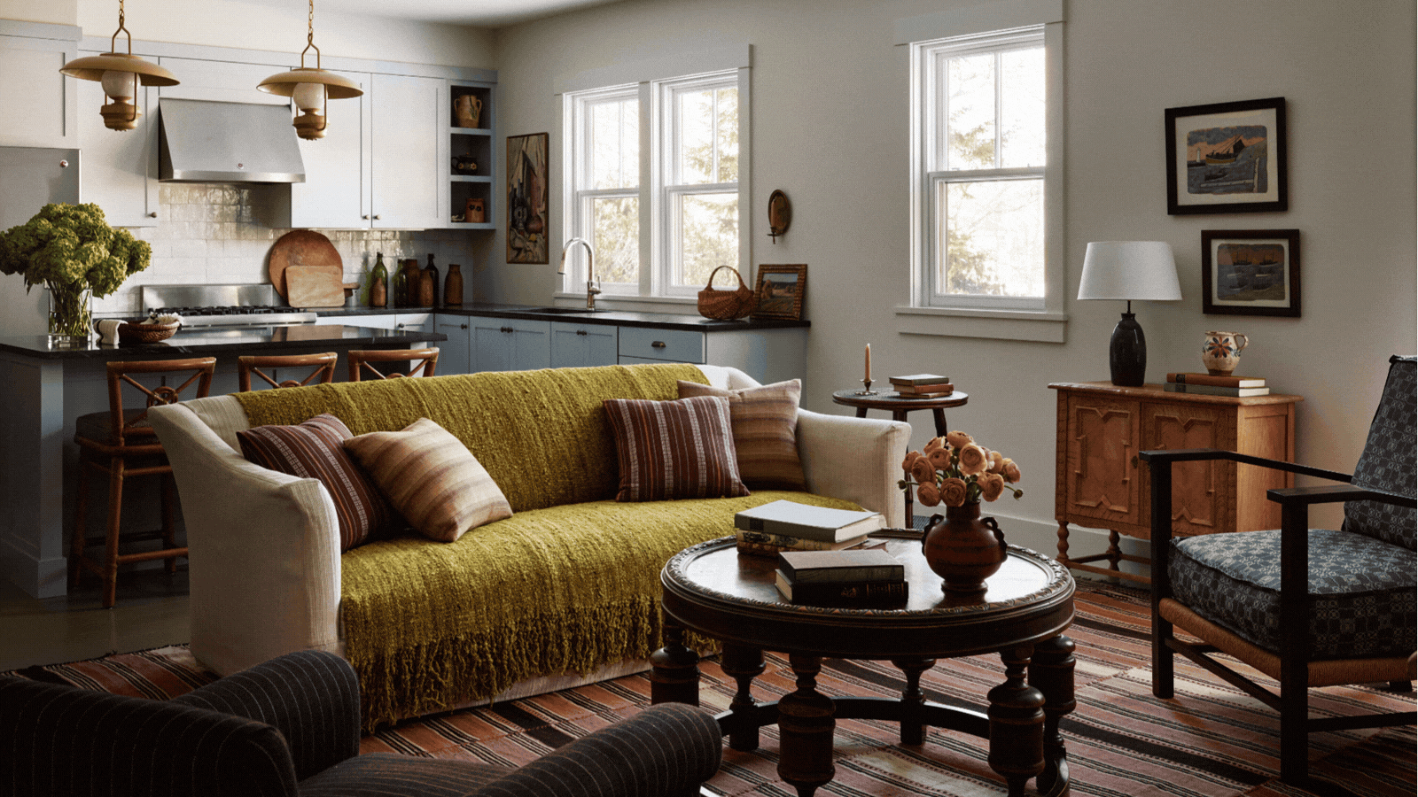 A GIF of three different New England-style rooms. There is a bedroom with patterned wallpaper, an open dining room with a white round table, and an open kitchen and living room with a yellow sofa