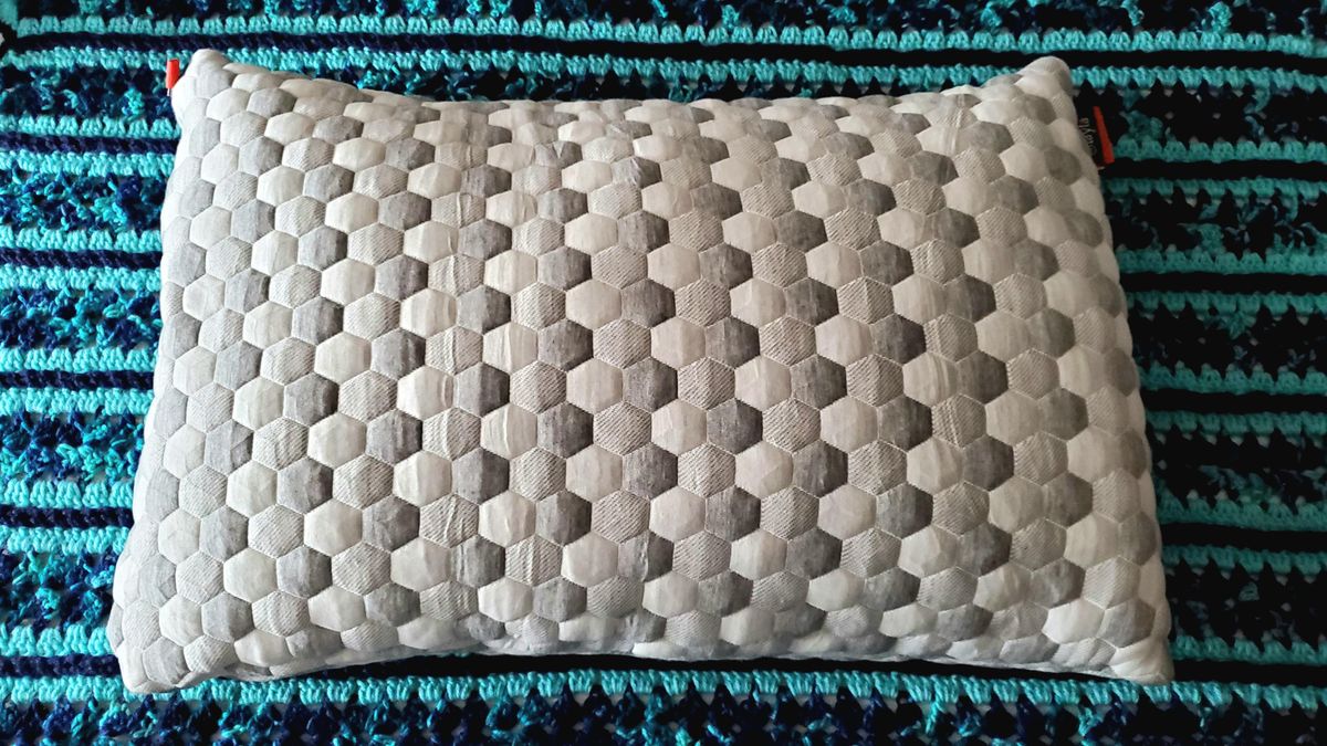 Image shows our Layla Kapok Pillow used during testing unpacked and placed on a blue bedroom rug ahead of testing