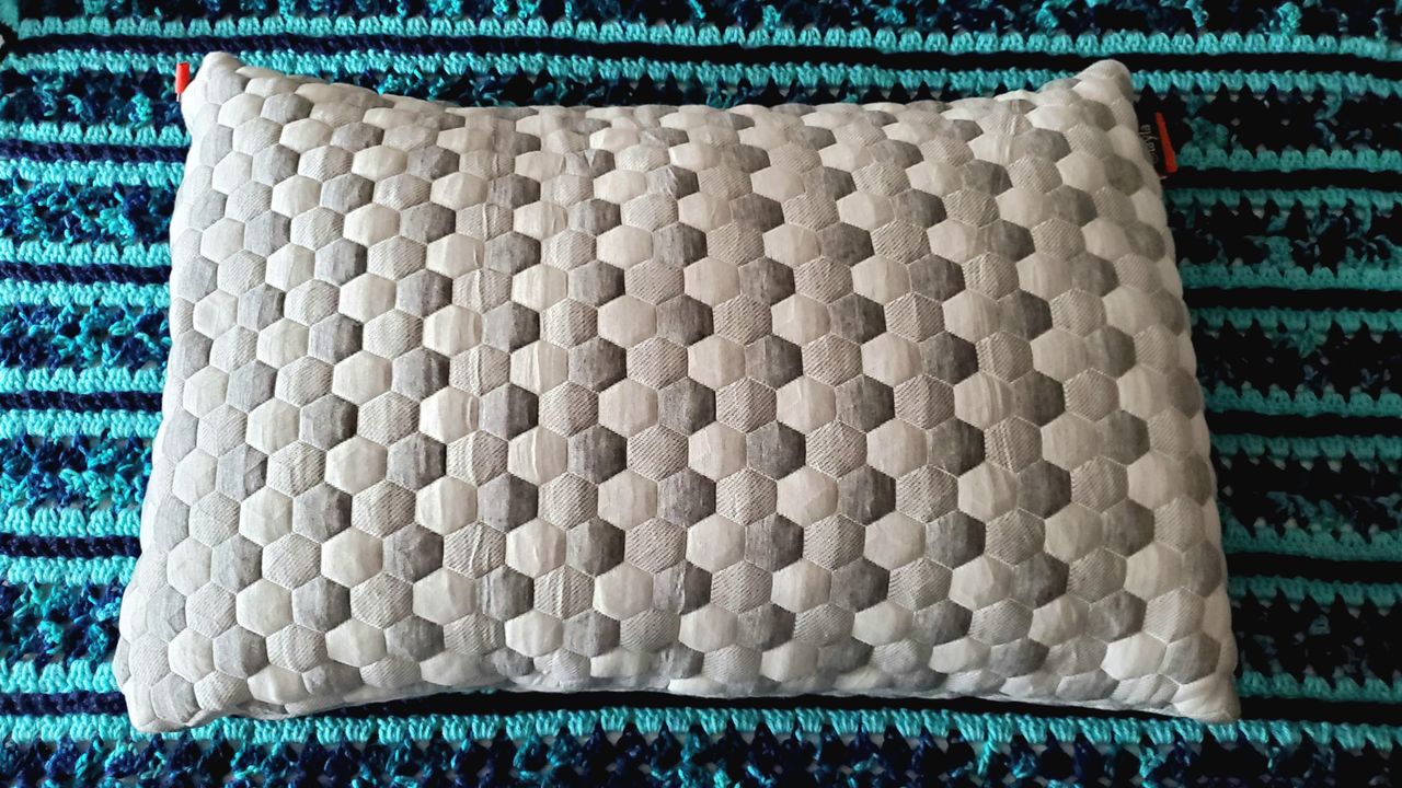 Image shows our Layla Kapok Pillow used during testing unpacked and placed on a blue bedroom rug ahead of testing
