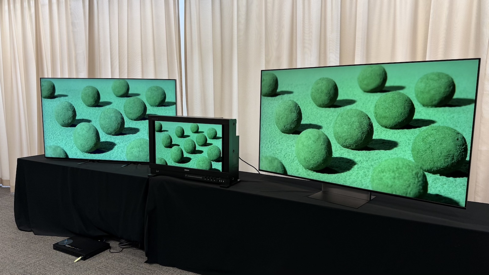The Sony Bravia 9 II and Bravia 9 TVs, and the Sony BVM-HX3110 mastering monitor, photographed on a black desk, with Sony demo footage on the screens