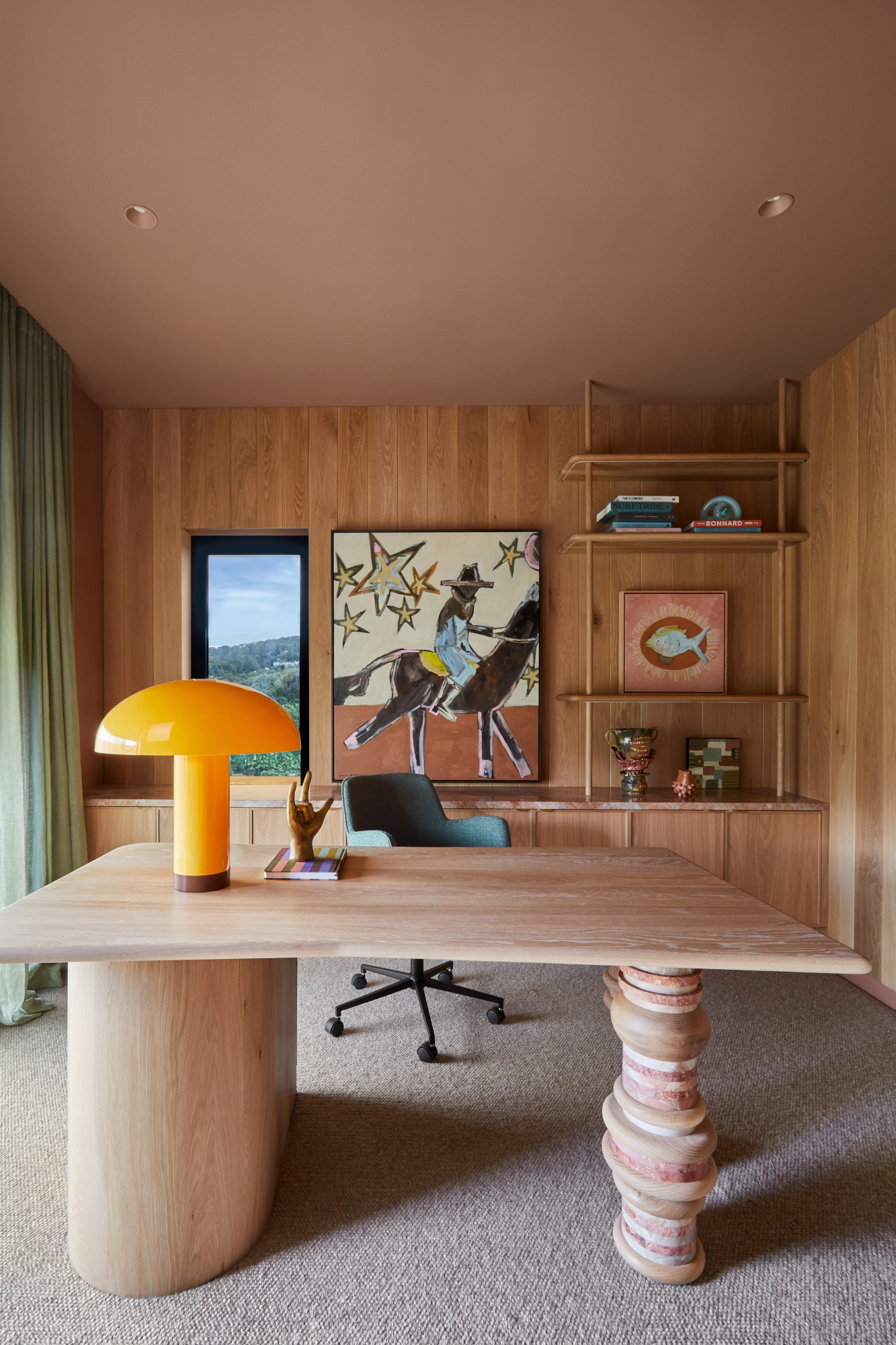 Home office with wood-clad walls, pink ceiling, pink marble stacked leg desk and orange lamp