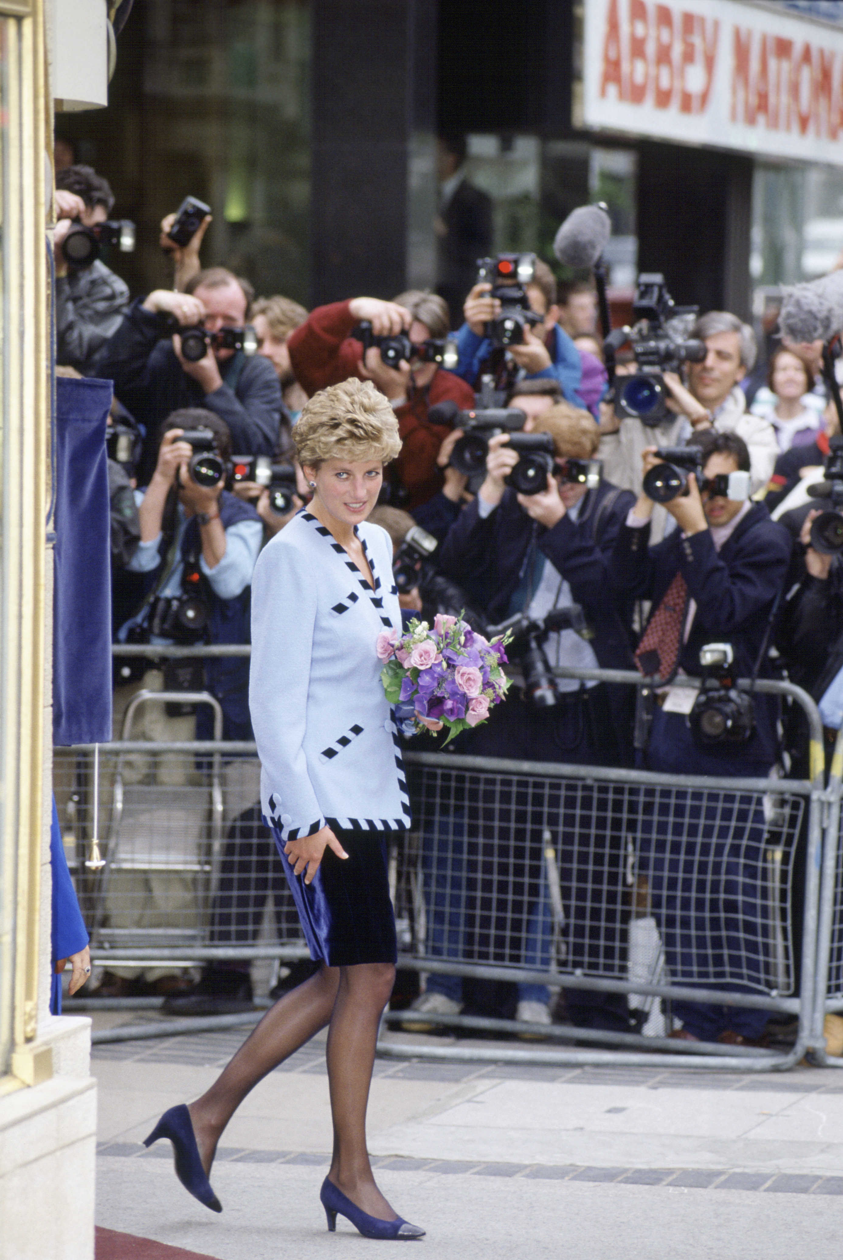 Princess Diana wearing a black and white suit surrounded by photographers