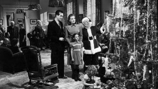 En svartvit stillbild från filmen Det hände i New York, där en familj står bredvid en jultome framför en stor julgran.