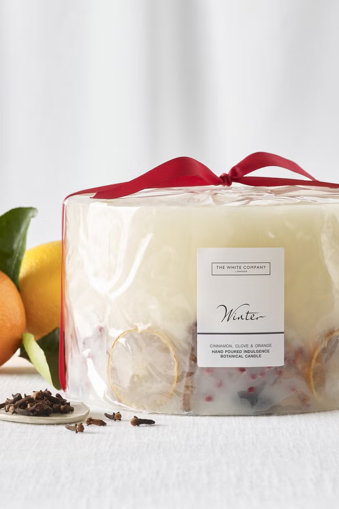 A white inclusion candle beside some lemons and cloves