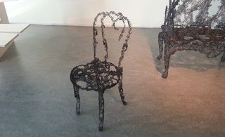 A chair made out of tiny black metal circles looks like it's incomplete.