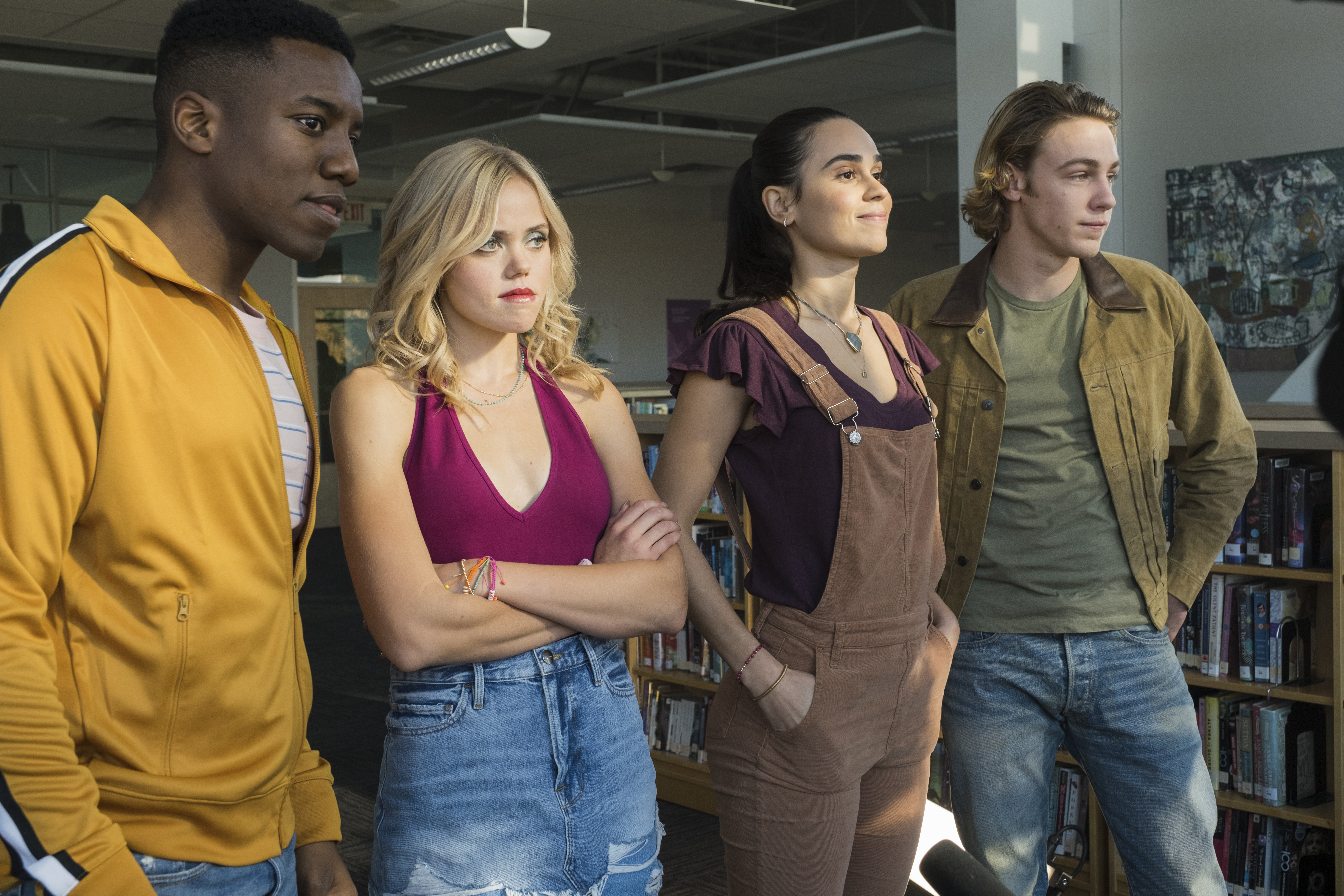 a group of teenagers stand around a school library in a still from the peacock teen show one of us is lying
