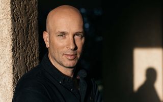 a bald man in a black shirt stands against a pillar