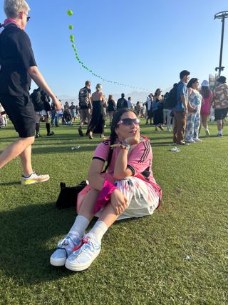 The Coachella influencer wears a pink T-shirt, white midi skirt, and custom Adidas sneakers with straps.