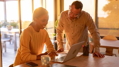 A couple smile as they look at a laptop together in their kitchen.