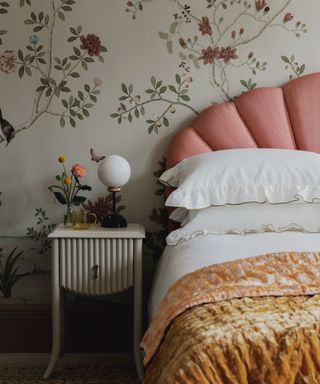 vintage wallpapered bedroom with a pink upholstered bed and vintage nightsand with fresh flowers