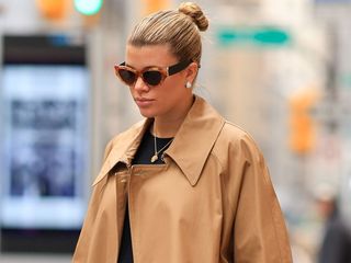 Sofia Richie Grainge wearing a tan trench coat, black shirt, and brown and black sunglasses