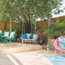 patio cover ideas, split level decking with bright furniture, hanging garden seat in corner under tree 