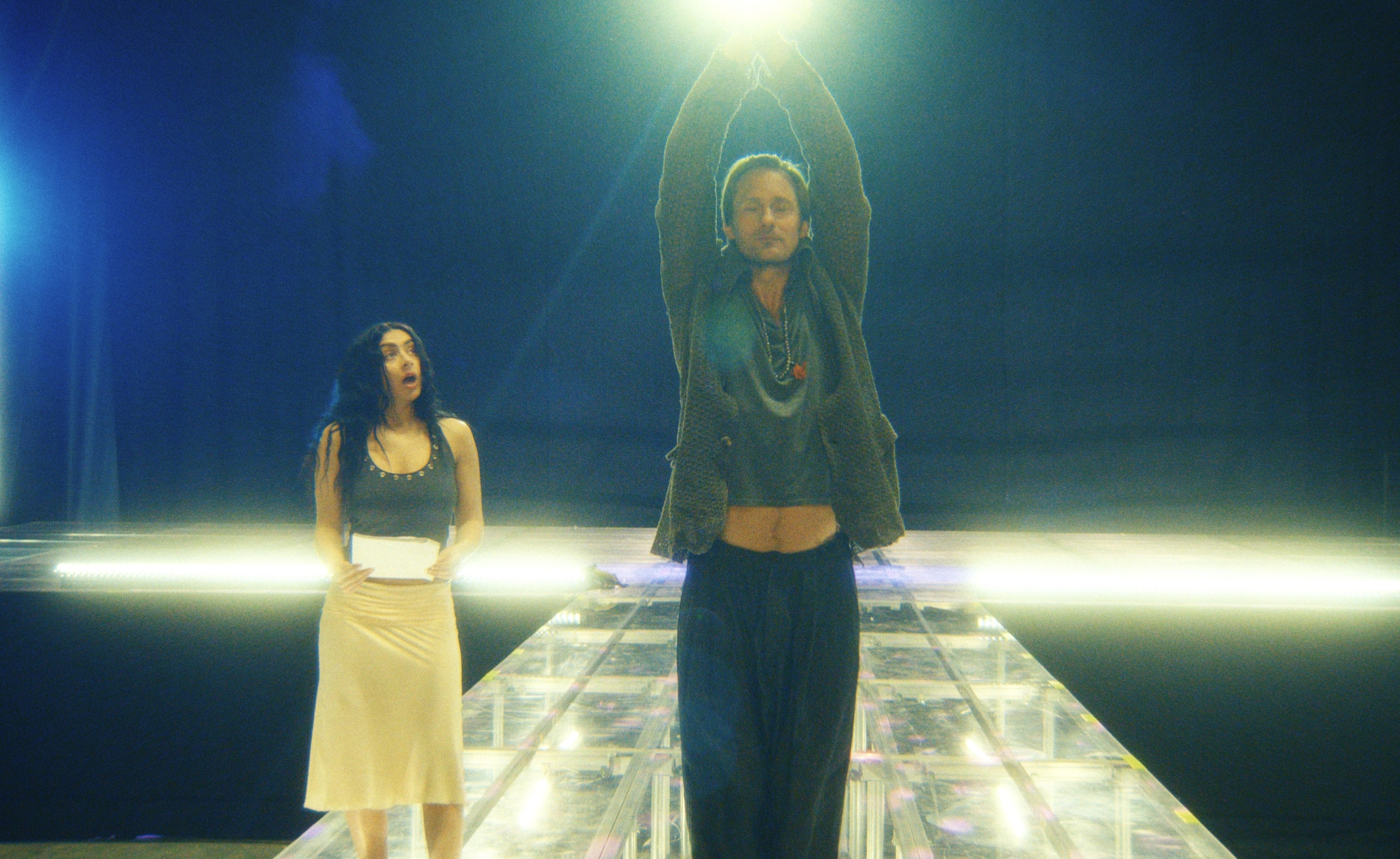 charli xcx looks surprised as alexander skarsgard as johannes lifts his arms above his head on a stage in a still from the movie the moment