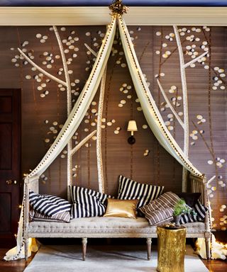 A daybed with fairy lights and a canopy in front of a brown wall