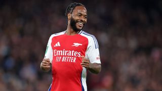 Raheem Sterling smiles on the pitch in his red and white Arsenal shirt.