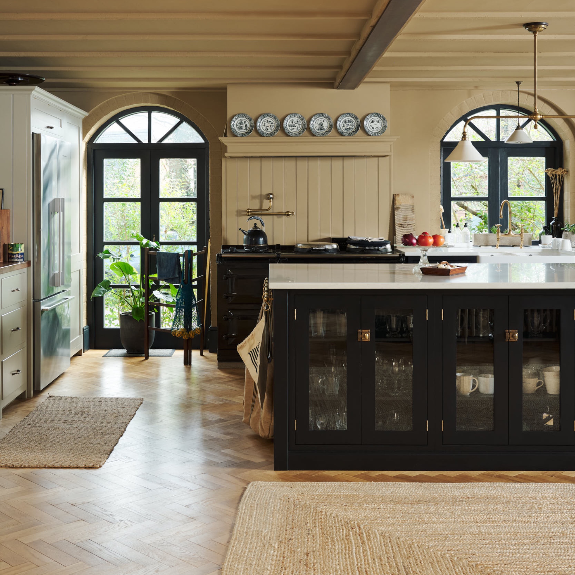ochre and black kitchen with black kitchen island with white worktops, parquet flooring with coir rugs, plates on shelf