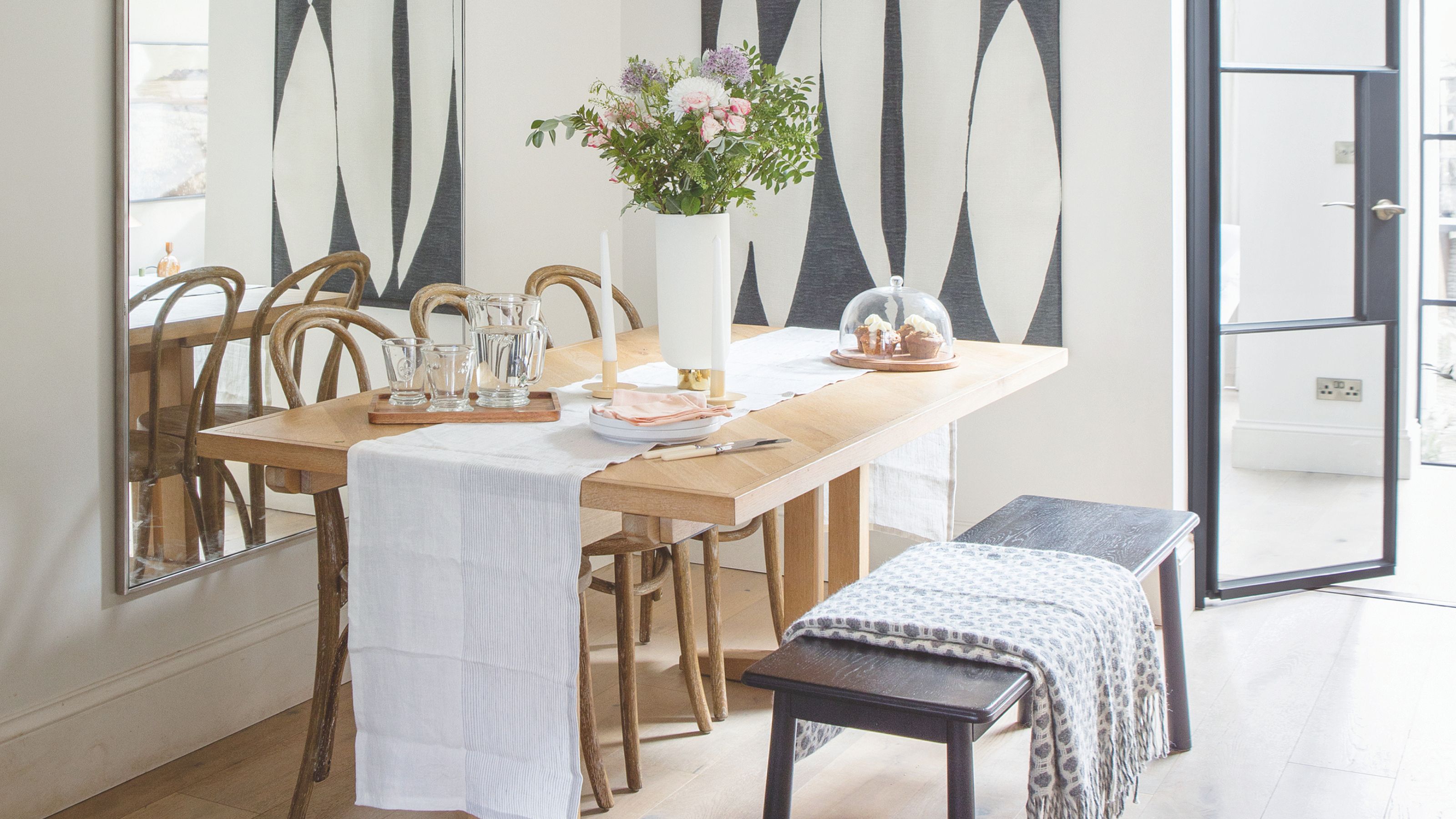 A light white-painted dining room with a rectangular wooden table, three chairs and a black dining bench