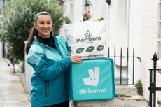 A Deliveroo delivery worker holding a Deliveroo-branded bag with Morrisons groceries inside.