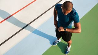 Man stands next to running track looking at running watch