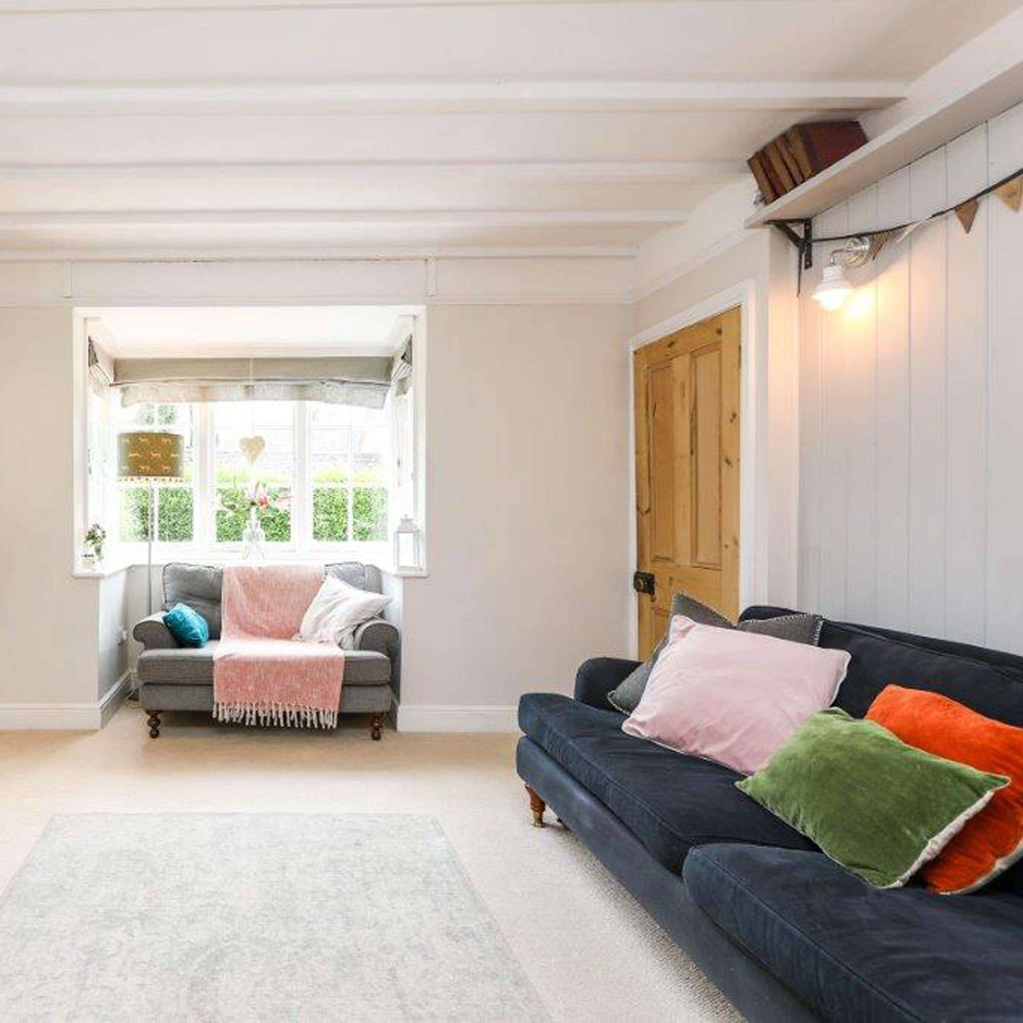 living room with grey wall panelling and bay window with grey loveseat