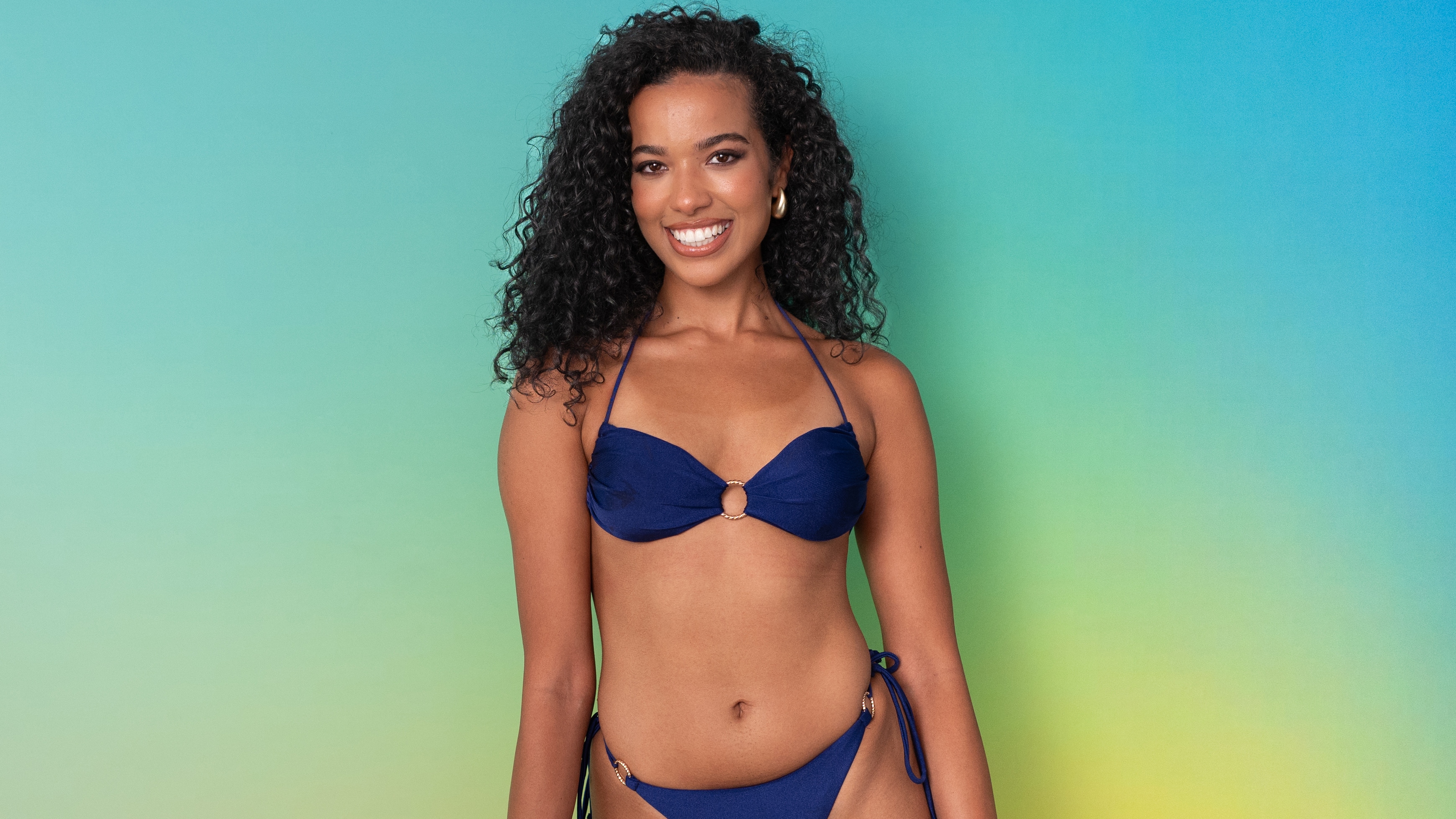 Yasmin standing in swimwear in front of a green background.