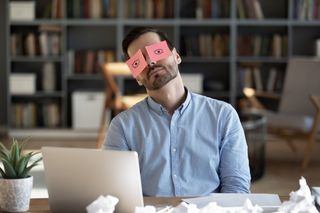 Man sleeps at desk with post-it notes on his eyes.