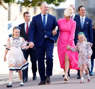 Mike Tindall wearing a blue suit holding hands with Zara Tindall, wearing a pink dress and holding hands with daughters Mia and Lena walking to church on Easter