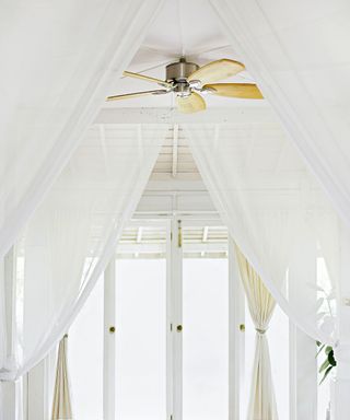 An all white bedroom with a light wood ceiling fan