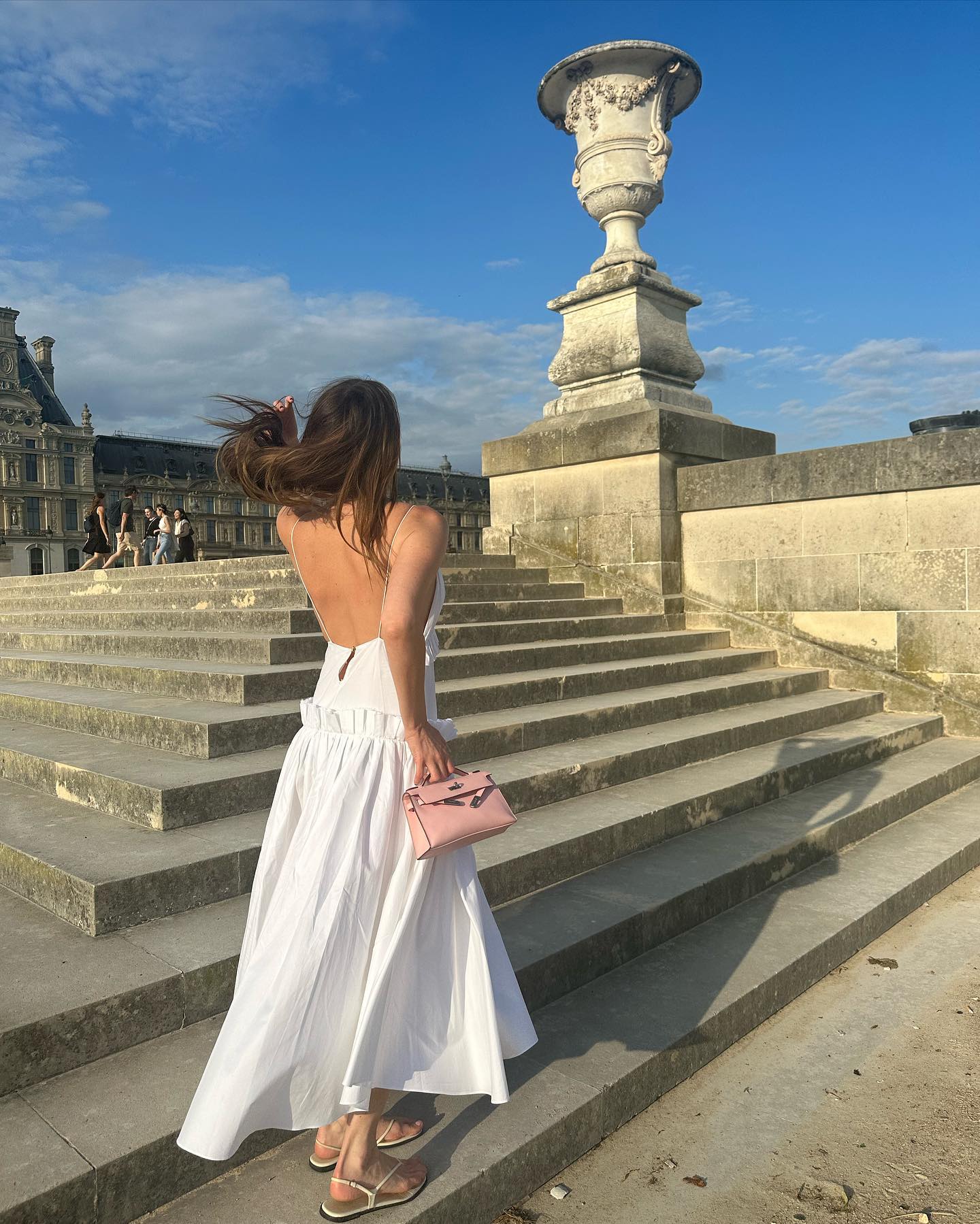 Camille Charriere wearing a white sundress with a pink Hermès bag and flat sandals.