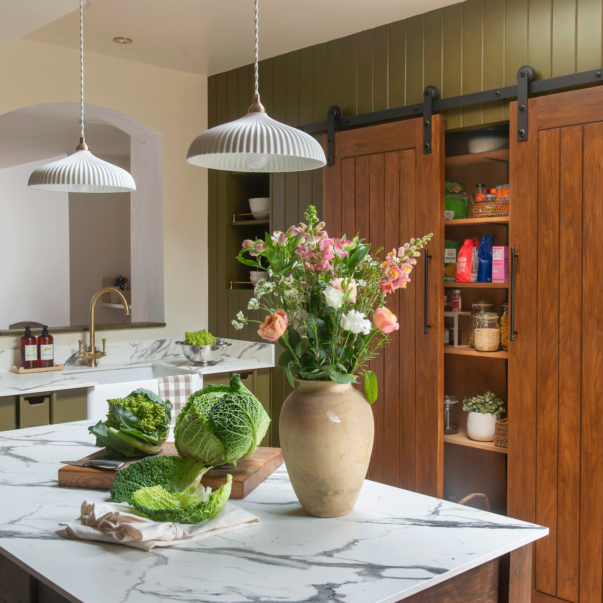a green kitchen with a marble counter top and kitchen island with a pantry with barn doors and an urn vase filled with flowers