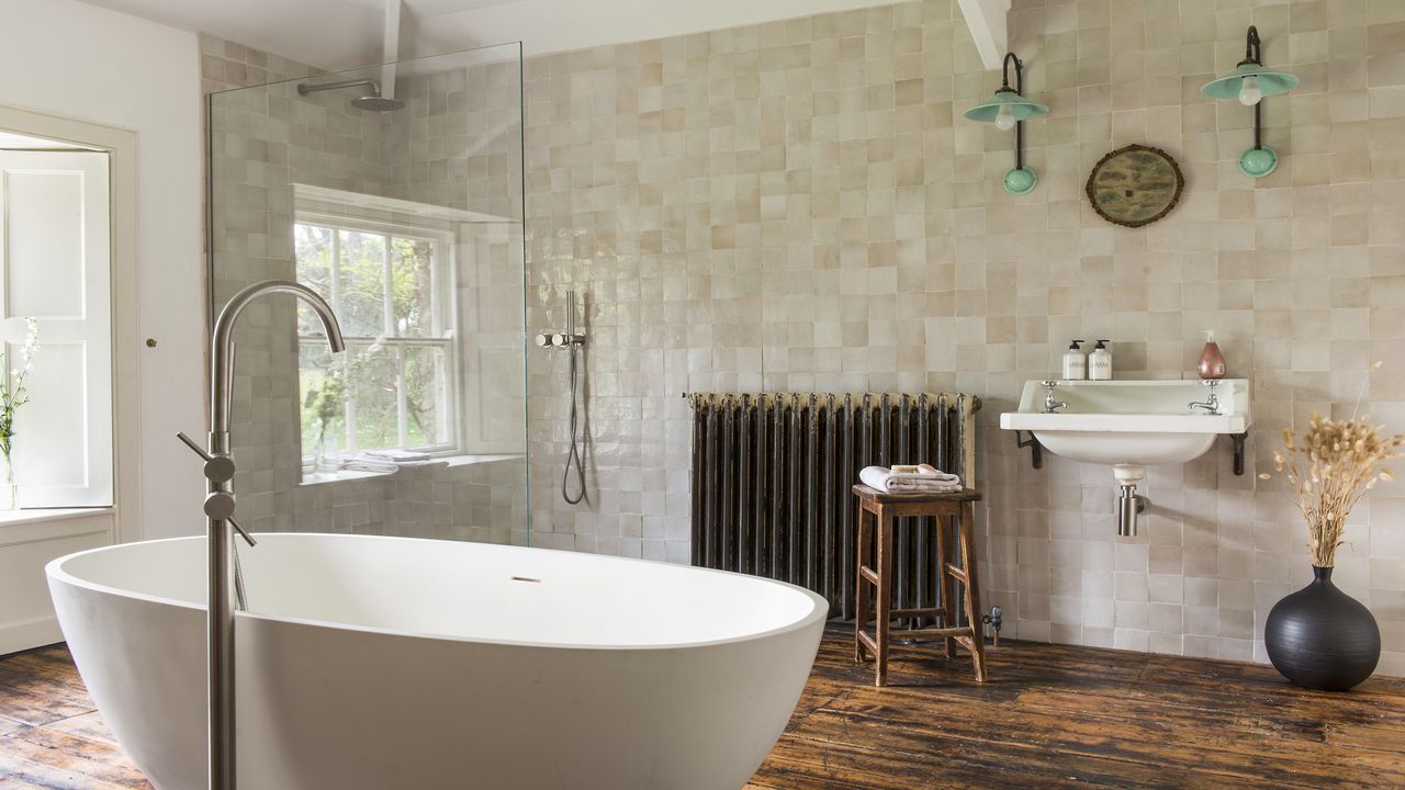 bathroom with beige bathroom tiles, white freestanding bath, wooden flooring, wooden stool and white basin