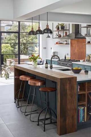 blue and white kitchen with white countertops, island, wooden breakfast bar, industrial style pendant lights, open hanging shelving