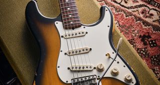 A close-up of a 1969 Fender Stratocaster sitting on a tweed hardshell guitar case.