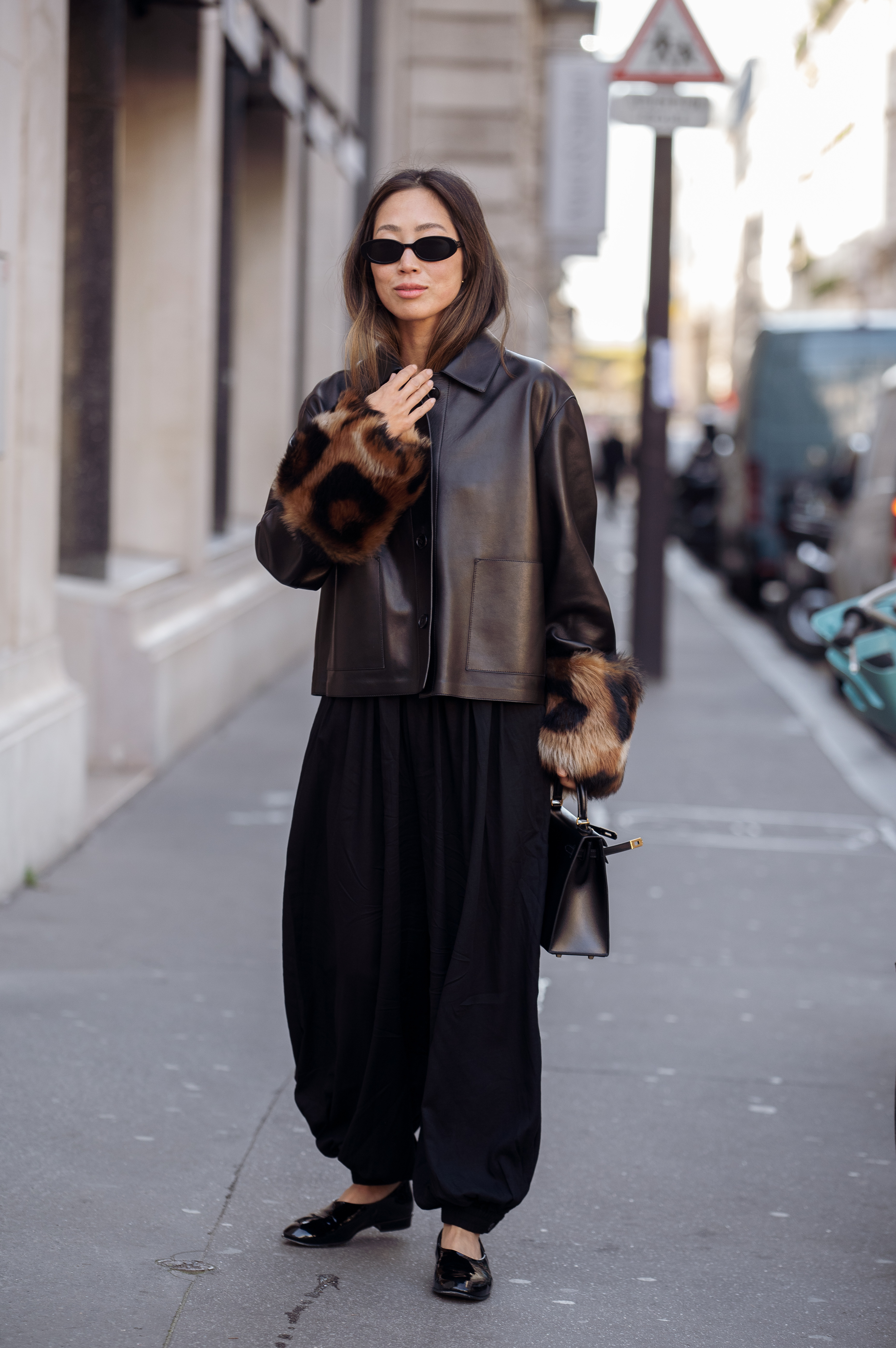 Aimee Soong wears a black leather jacket with fur-trimmed sleeves over a black wide-leg jumpsuit, styled with black patent flats, a black handbag, and slim black sunglasses outside The Row shows during the Womenswear Spring Summer 2026 as part of Paris Fashion Week on October 02, 2025 in Paris, France.