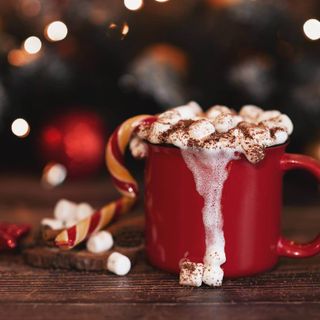 A large red mug filled with hot chocolate, cream, marshmallows and a candy cane.