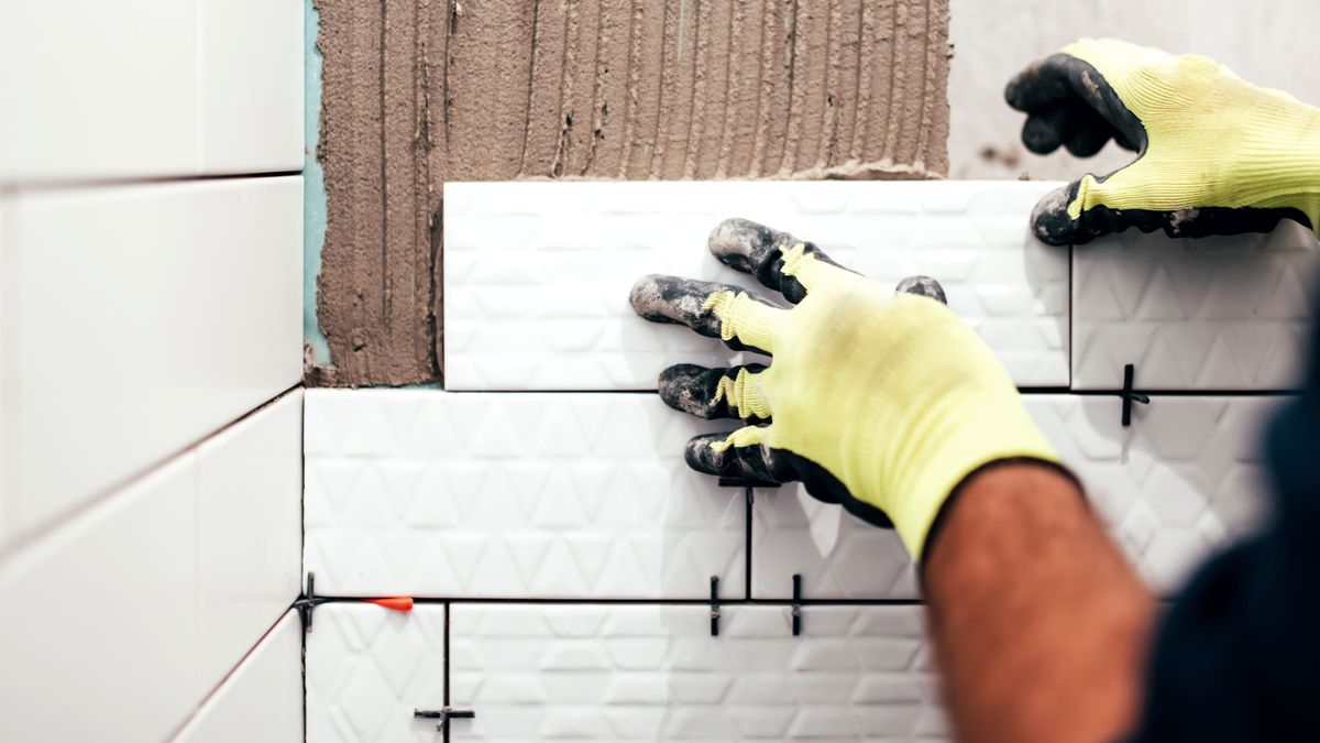 Hand placing white tile near corner on wall