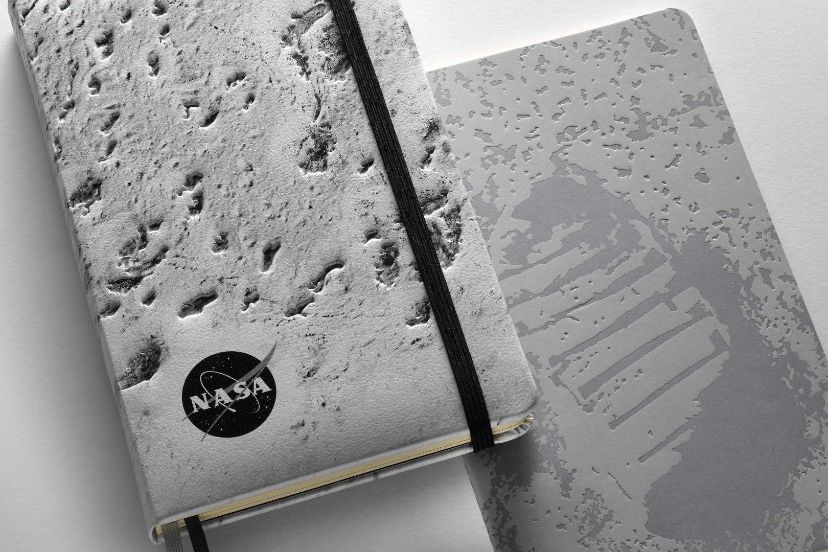 NASA-inspired Limited Edition Notebooks from Moleskine. Left: Hardcover notebook with close up of the moon's surface on the front cover, black and white NASA logo in bottom left cover. Right: Softcover with Neil Armstrong's footprint on the moon on the front cover.