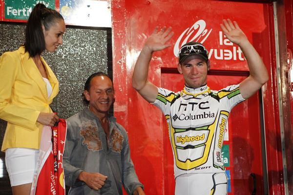 Mark Cavendish steps onto the podium to take the leader's jersey