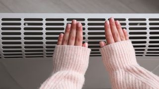 Woman warming hands near electric heater at home