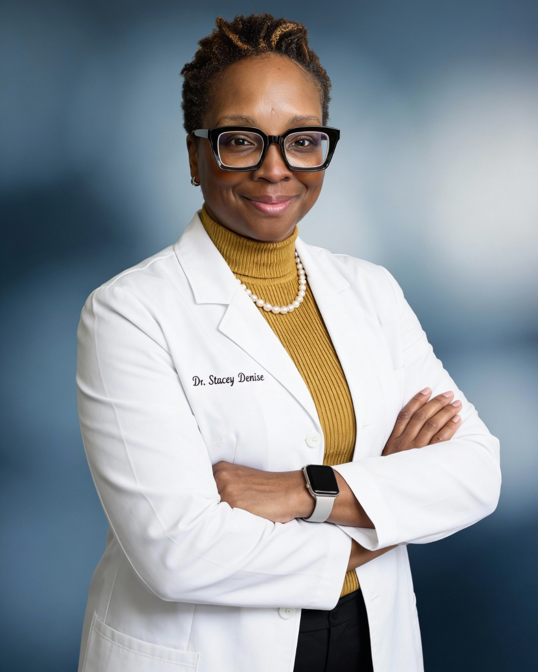 A headshot of a black woman with glasses wearing a dr's overcoat