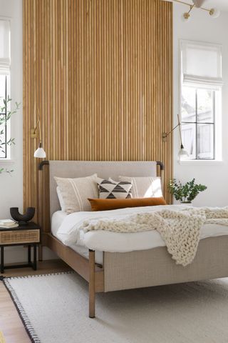 neutral modern bedroom with cladding behind bed, wall lights, cream rug, modern bed with wood and upholstery, knitted blanket, plants, nightstands