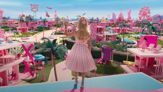 Bright pink barbie dream world with Barbie waving in a pink plaid dress.