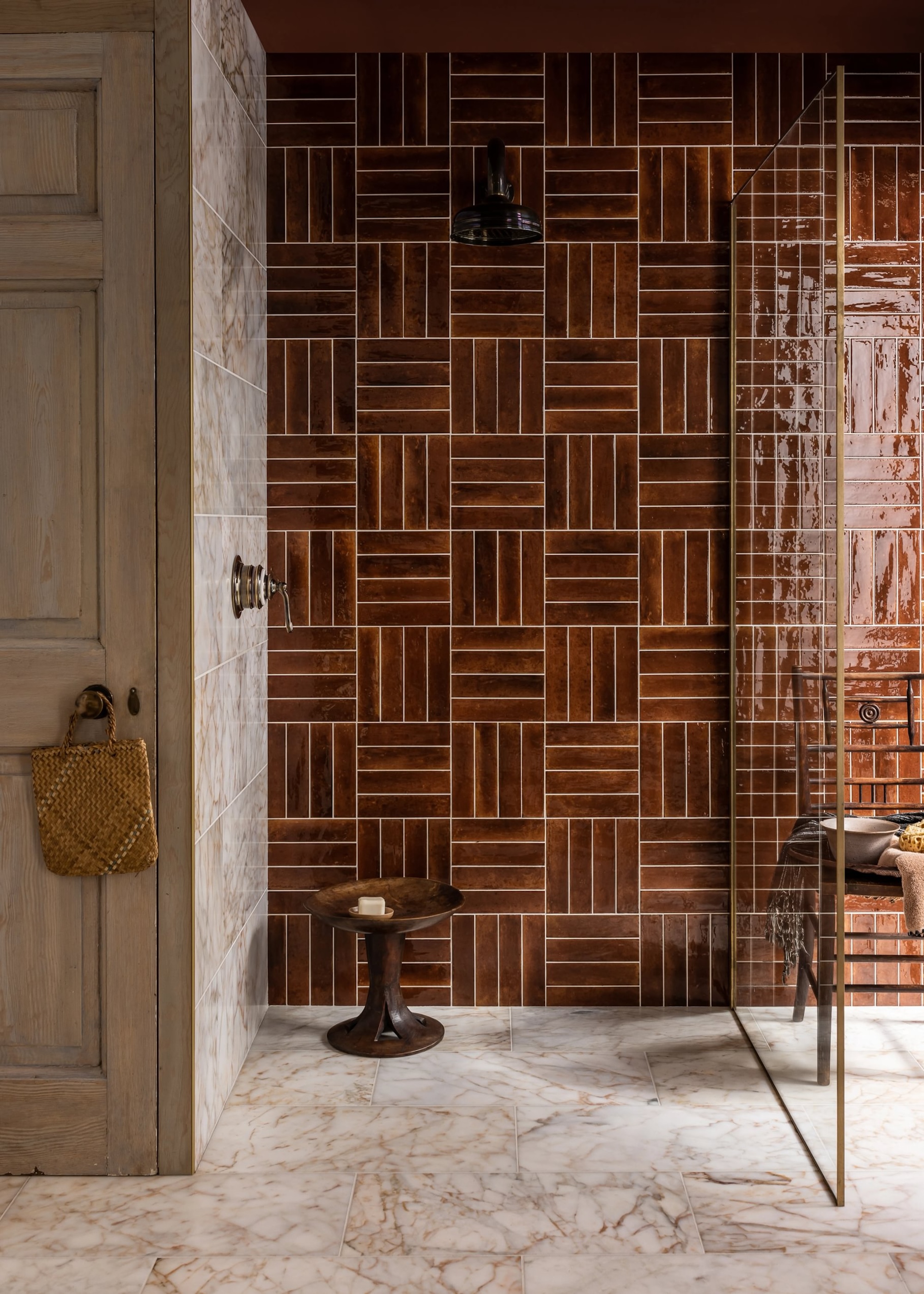 a walk in shower with toffee colored tiles and a brown and beige marble floor and gold trimmed shower screen
