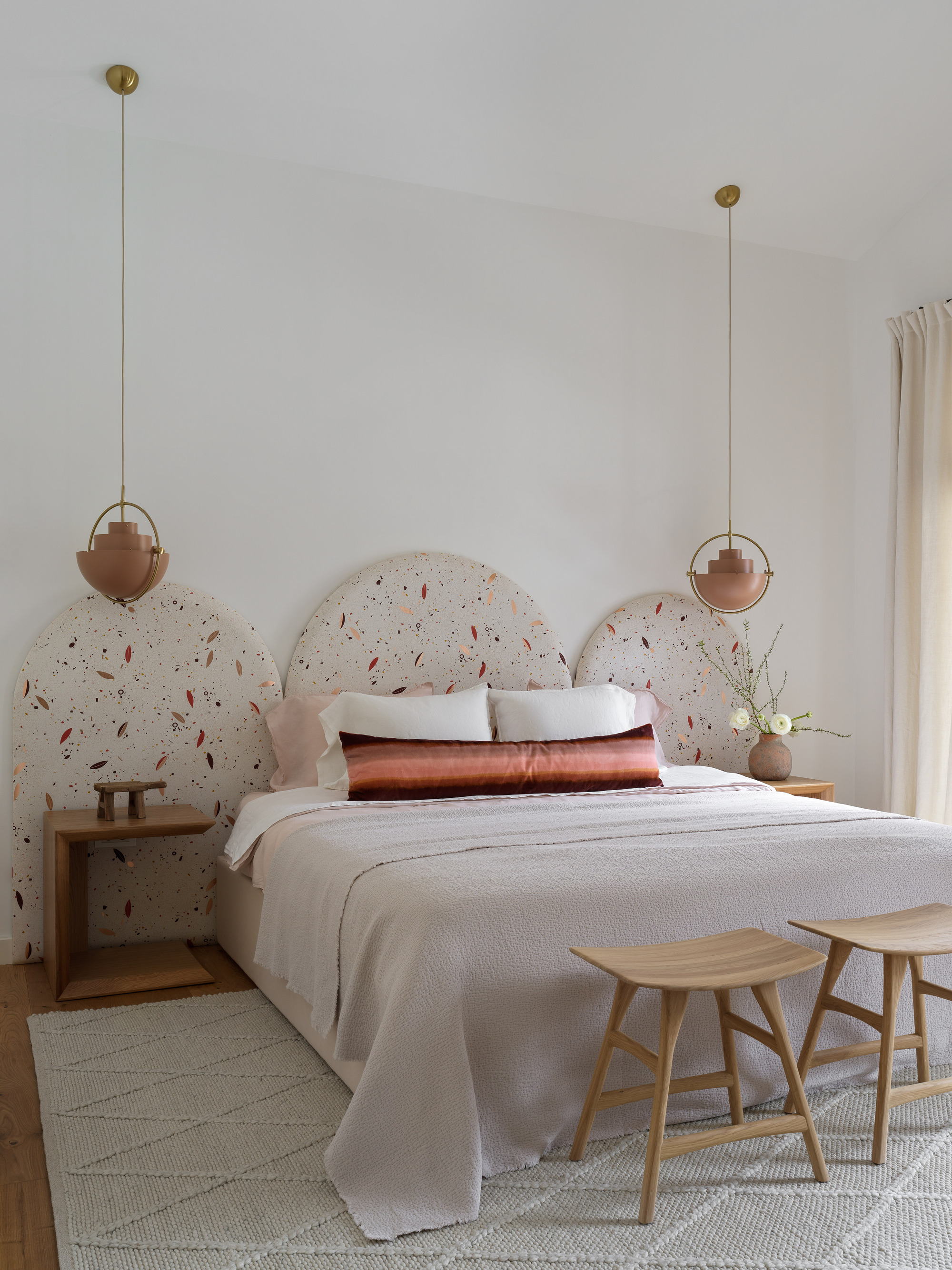 modern bedroom with arched upholstered bedhead, two pendant lights hanging over bedside table, two side tables at the end of the bed