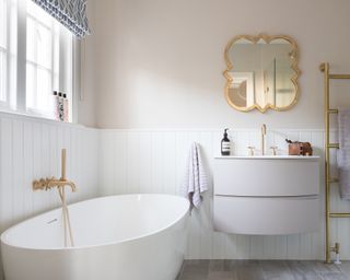 An ideas for a small bathroom showing a white panelled wall with soft pink paint, white furniture and brushed gold fittings